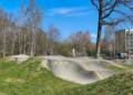 Pista de skatepark con rampas de hormigón y una zona de pumptrack con curvas peraltadas en un espacio al aire libre